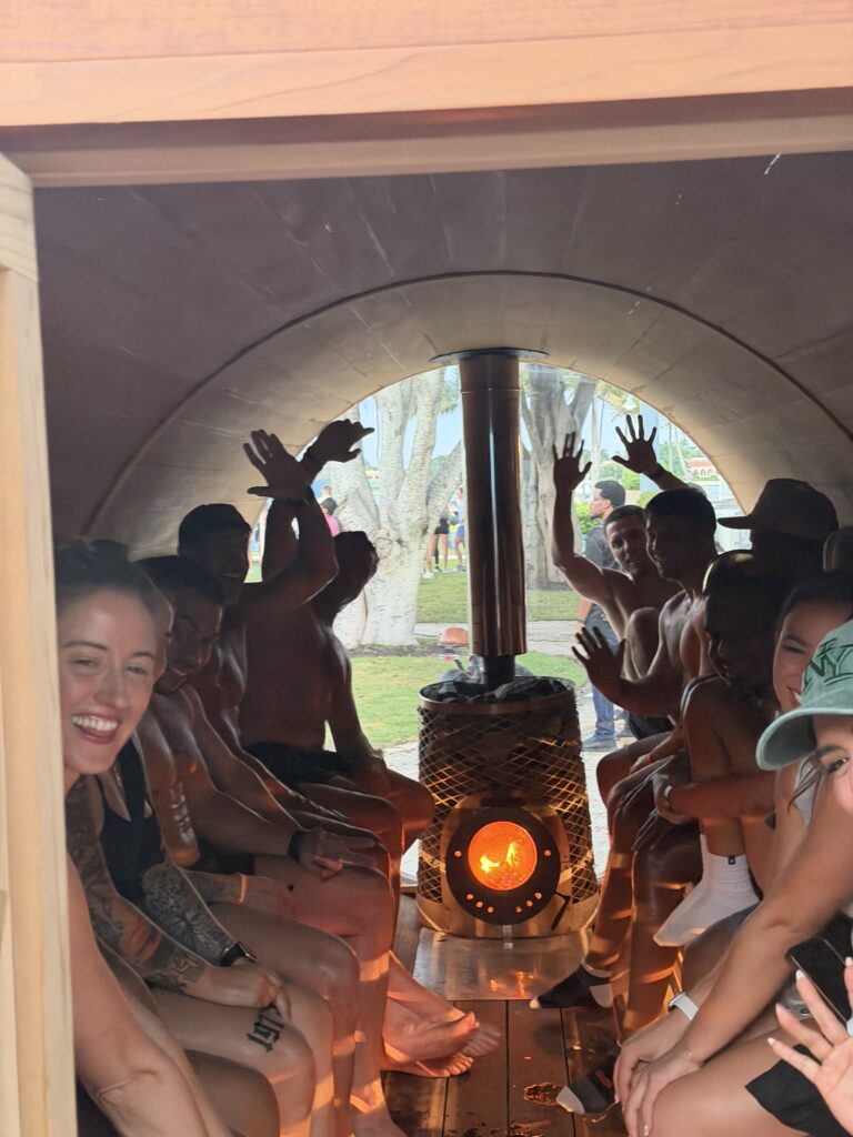 People riding in a covered train car, seated on both sides, raising their hands around a glowing central heater.